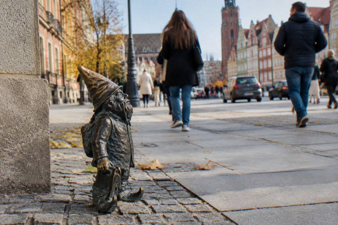 Small bronze dwarf statue on a city street with people walking past