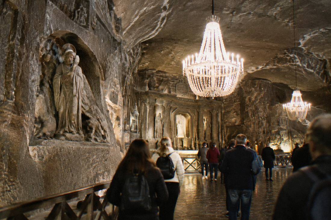 Interior of a salt mine chapel carved from salt with chandeliers and visitors on a walkway