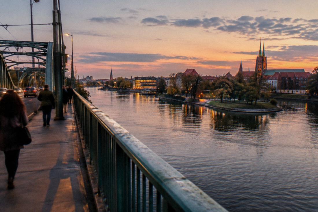 Bridge over the Odra river at dusk with riverside buildings lit up