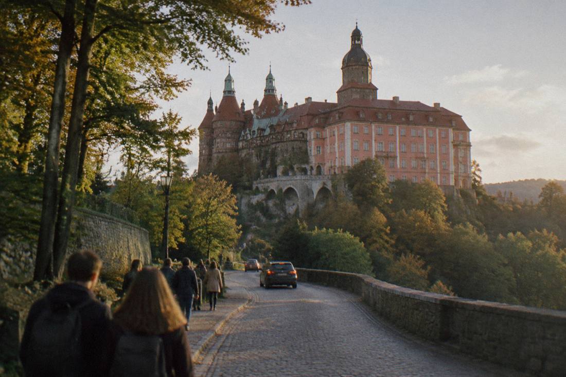 A forest road leading up to a large castle complex on a hilltop in Poland