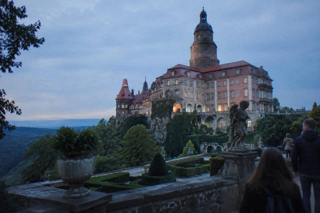 The stone facade and tower of a large castle seen from its garden terraces in Poland