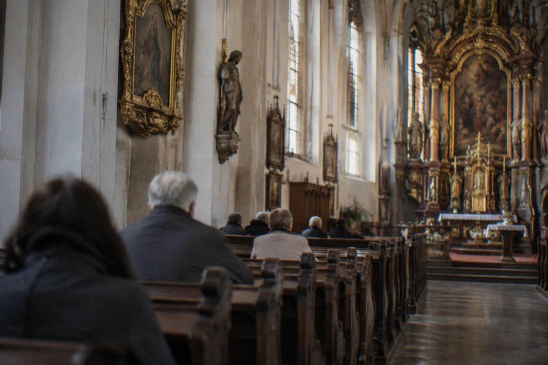 An ornate church interior with wooden pews and warm light through windows