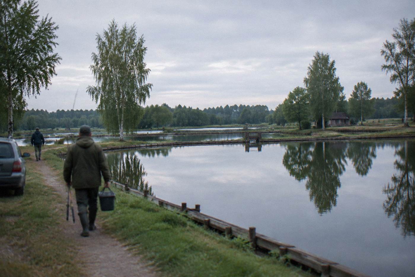 Wide view over calm fish ponds with wooden banks and trees reflected in still water