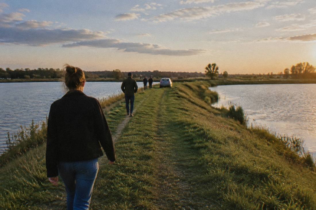 Grass-covered earthen dyke path running between two fish ponds under a wide sky