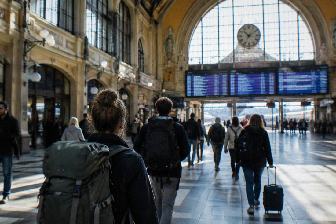 Travelers with backpacks walking through a grand railway station concourse with a departure board