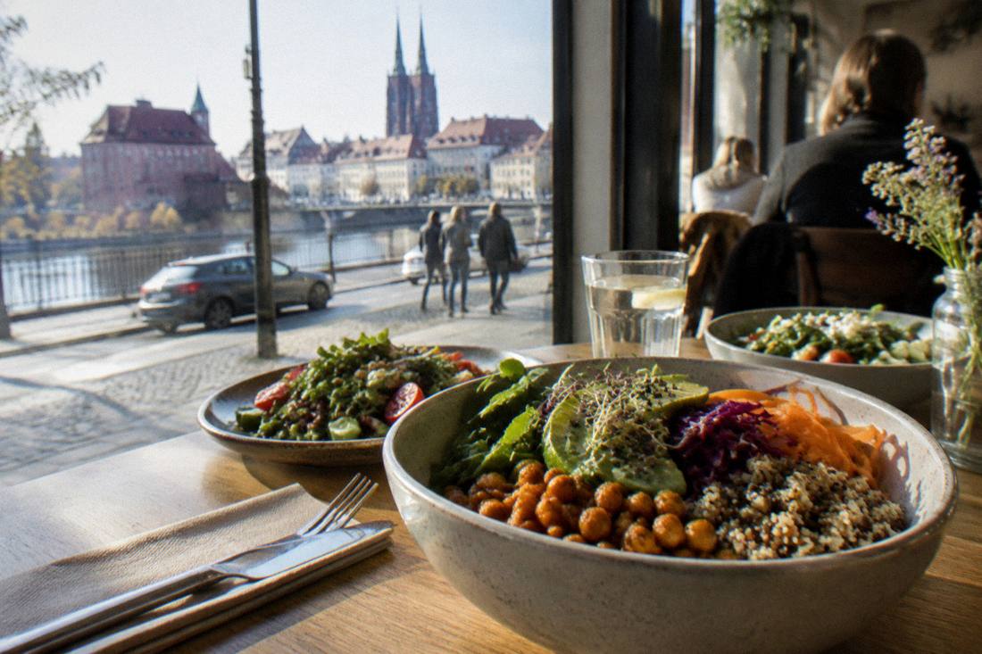 A colorful plant-based bowl and fresh salads on a cafe table by a window
