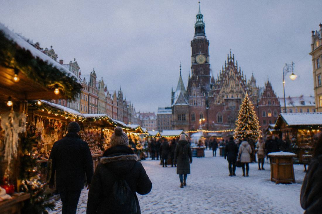 Festive wooden market stalls with string lights on a snowy old town square at dusk