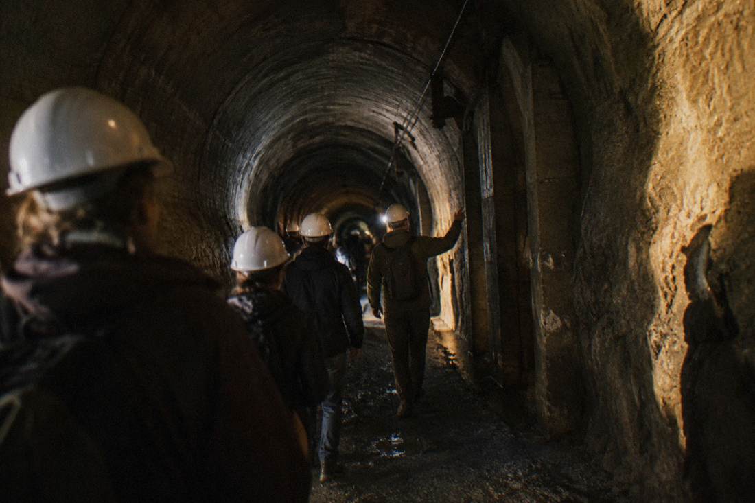 Guide leading a small group of visitors through a dim underground tunnel with helmets