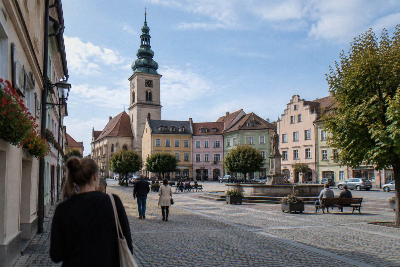 A small Lower Silesian town square with pastel townhouse facades and a church tower under a blue sky
