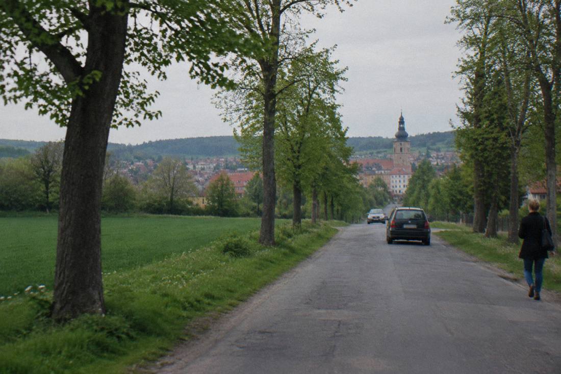A single-track country road lined with trees leading toward a distant town