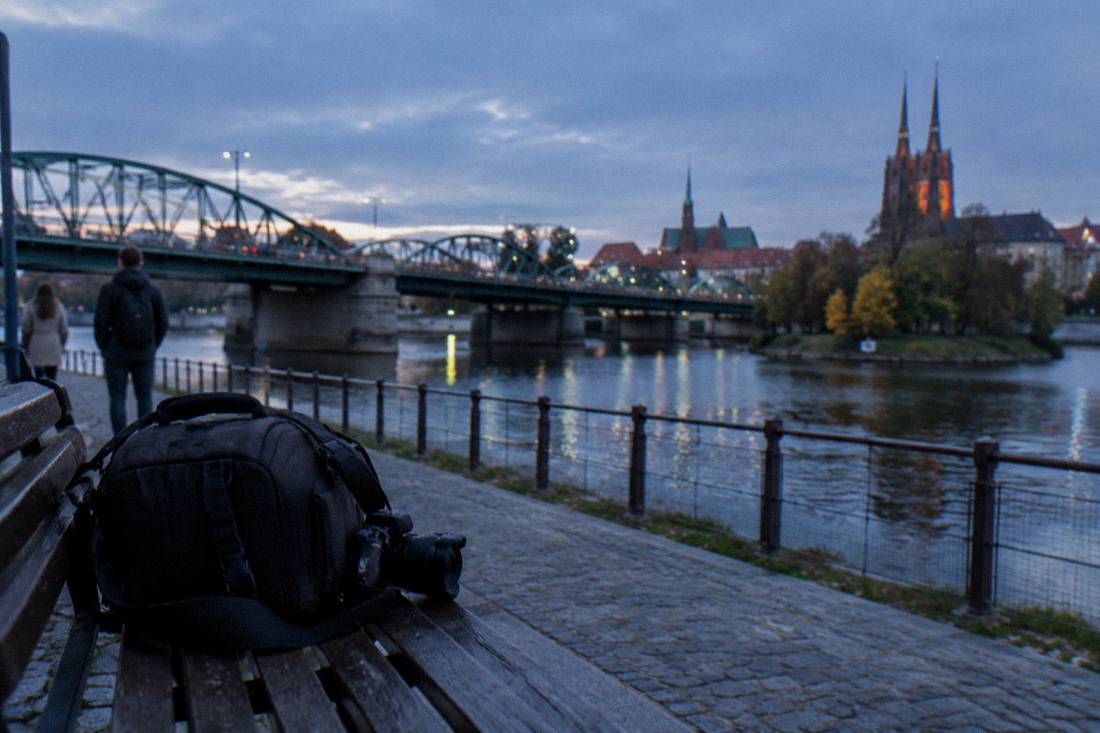 A photographer's camera bag on a bench beside the Odra river in Wroclaw