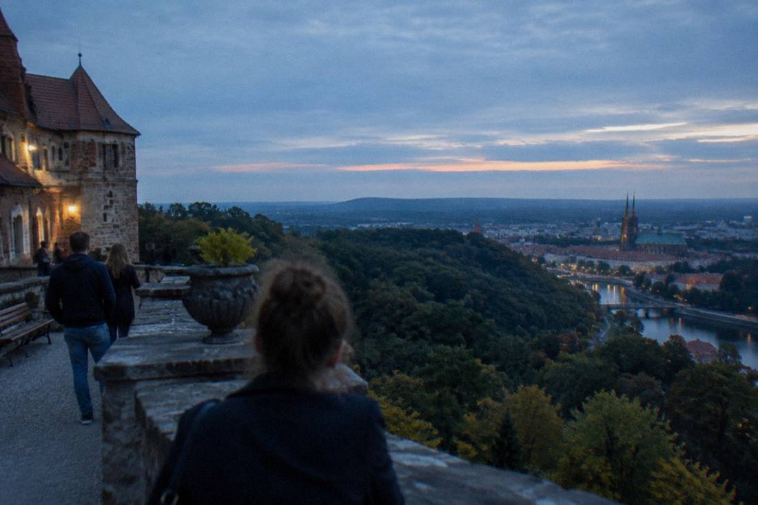 A hilltop castle terrace overlooking forested hills with a small town below
