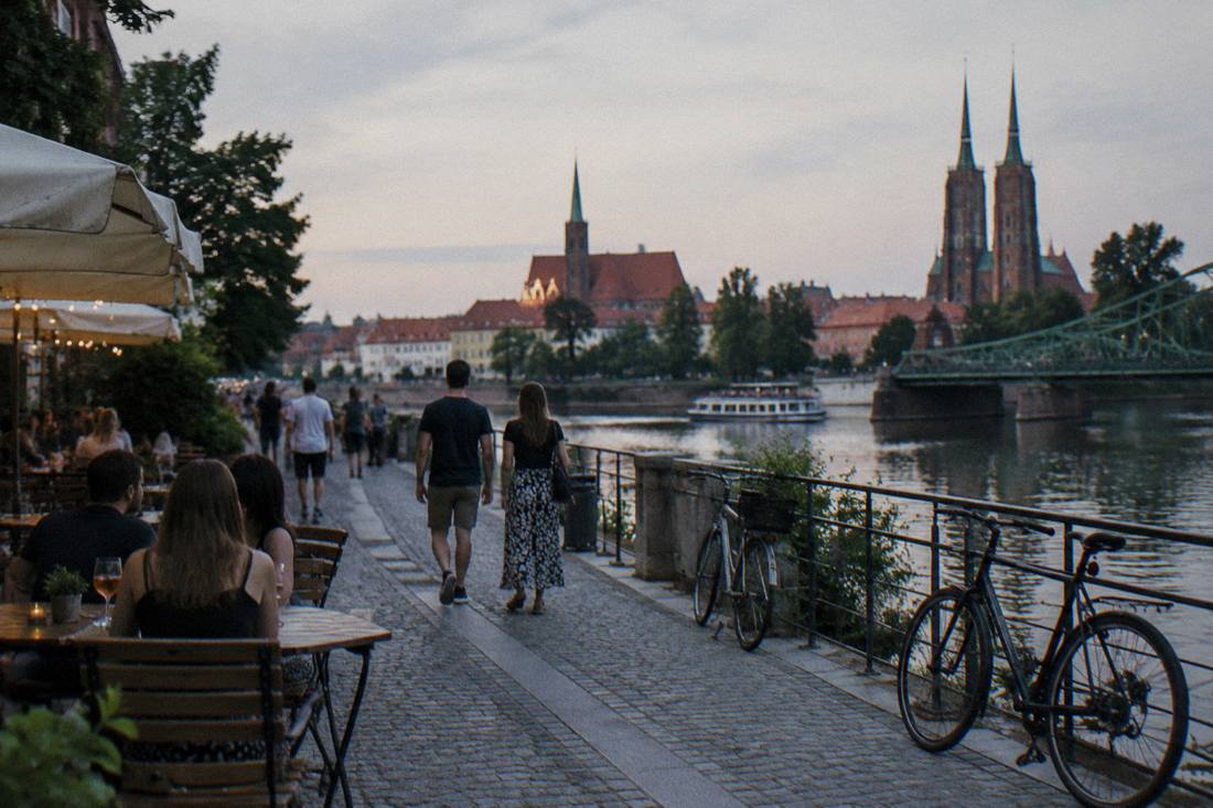 A riverside walking path with cafe tables and bicycles on a summer evening