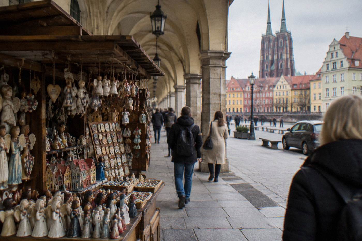A souvenir stall with handmade crafts displayed under a historic Wroclaw arcade