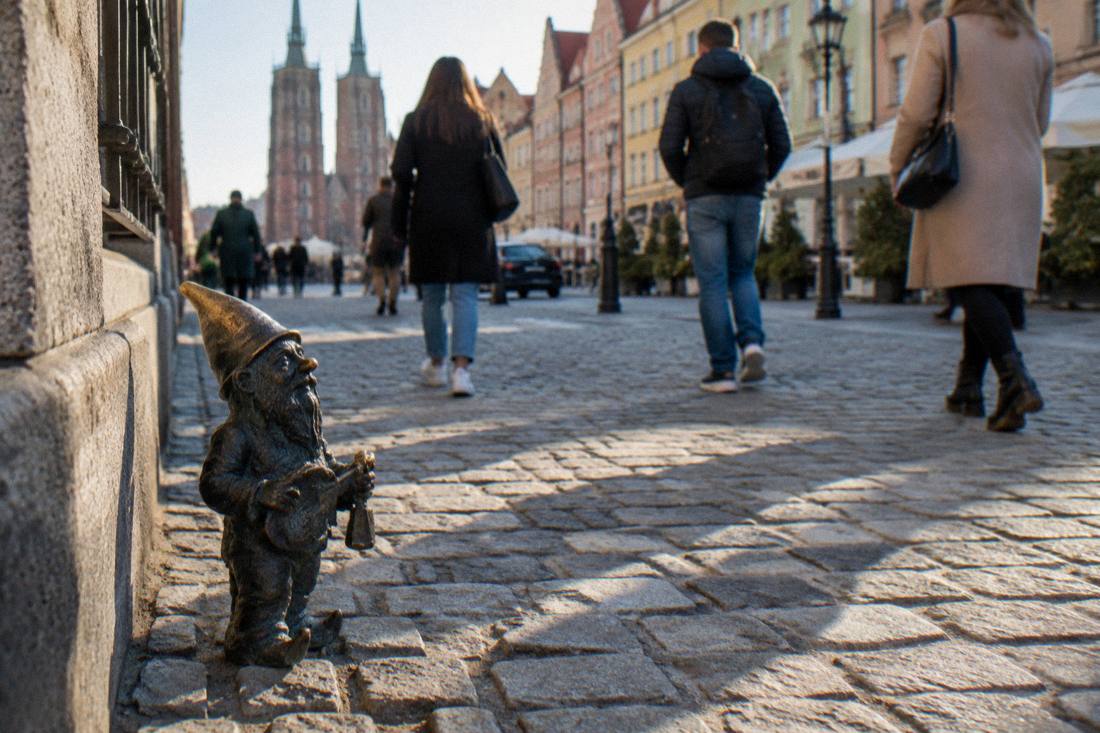 A bronze dwarf statuette on a Wroclaw cobblestone street with passersby nearby