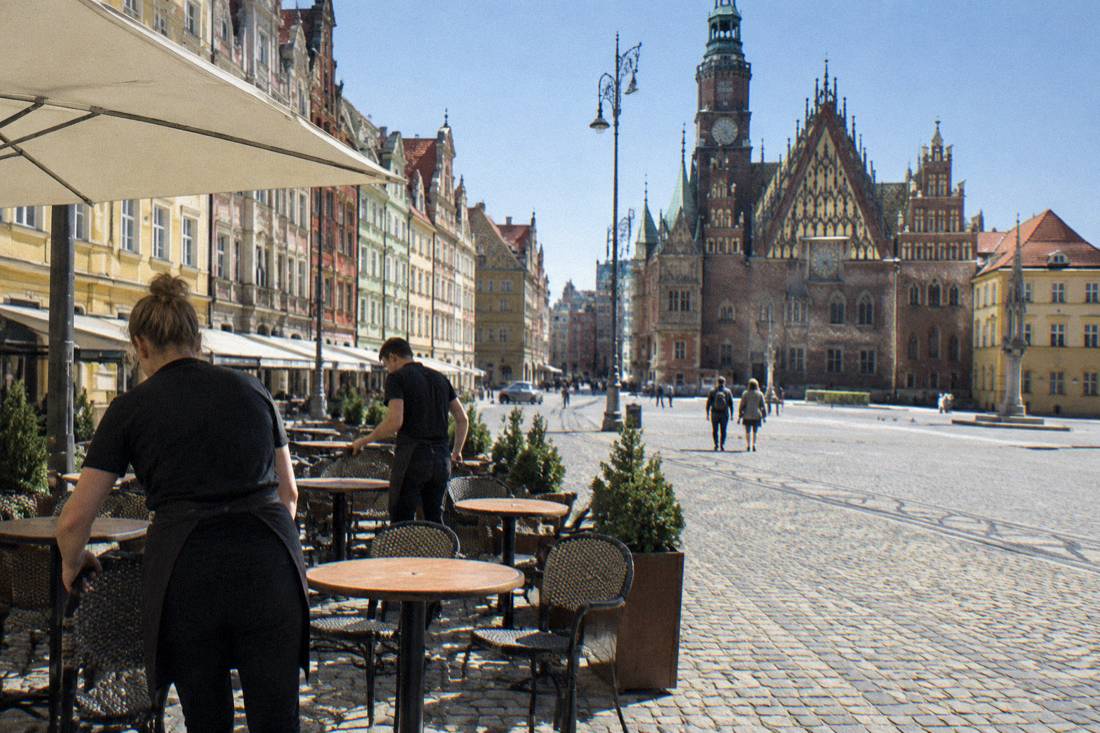 A café terrace on Wroclaw Market Square setting out chairs and tables while the square is still quiet