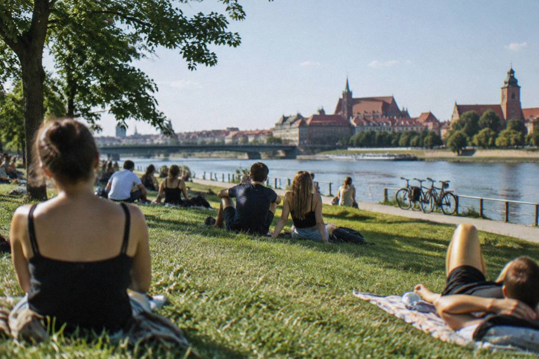 People relaxing on Slodowa Island grass beside the Odra river on a warm afternoon