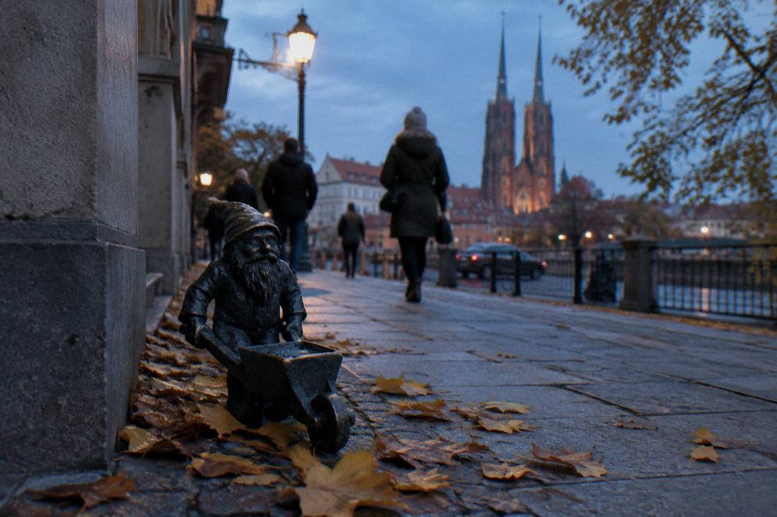 A dwarf statue on a Wroclaw sidewalk with autumn leaves around it