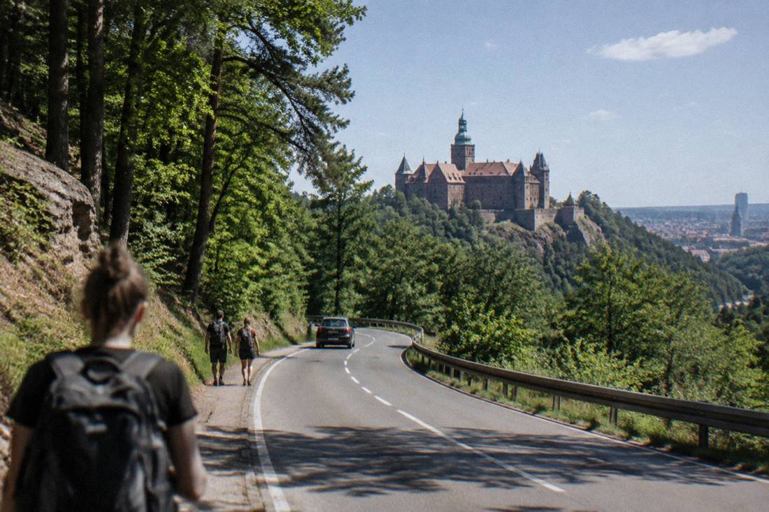 A forest road winding through wooded hills toward a large castle on a ridge