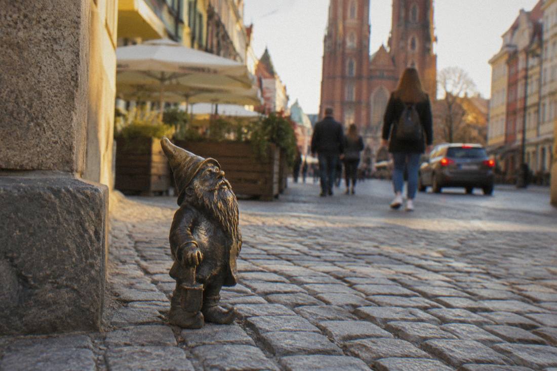 Small bronze dwarf statue standing on a cobblestone street in Wroclaw Old Town