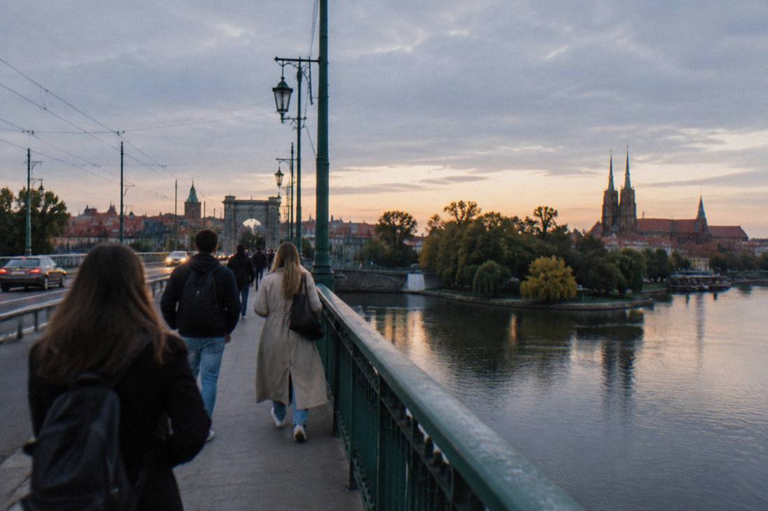 People walking across a bridge over the Odra river in Wroclaw at dusk