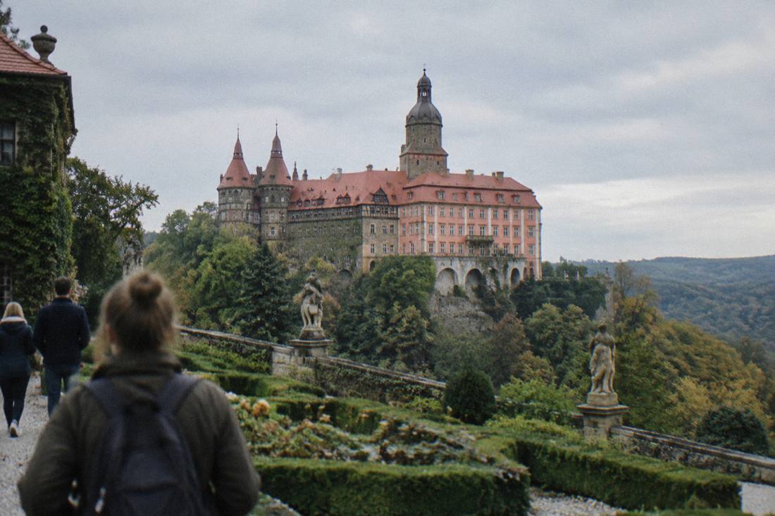 The large terracotta-roofed Ksiaz Castle seen from its gardens on a hillside above forest