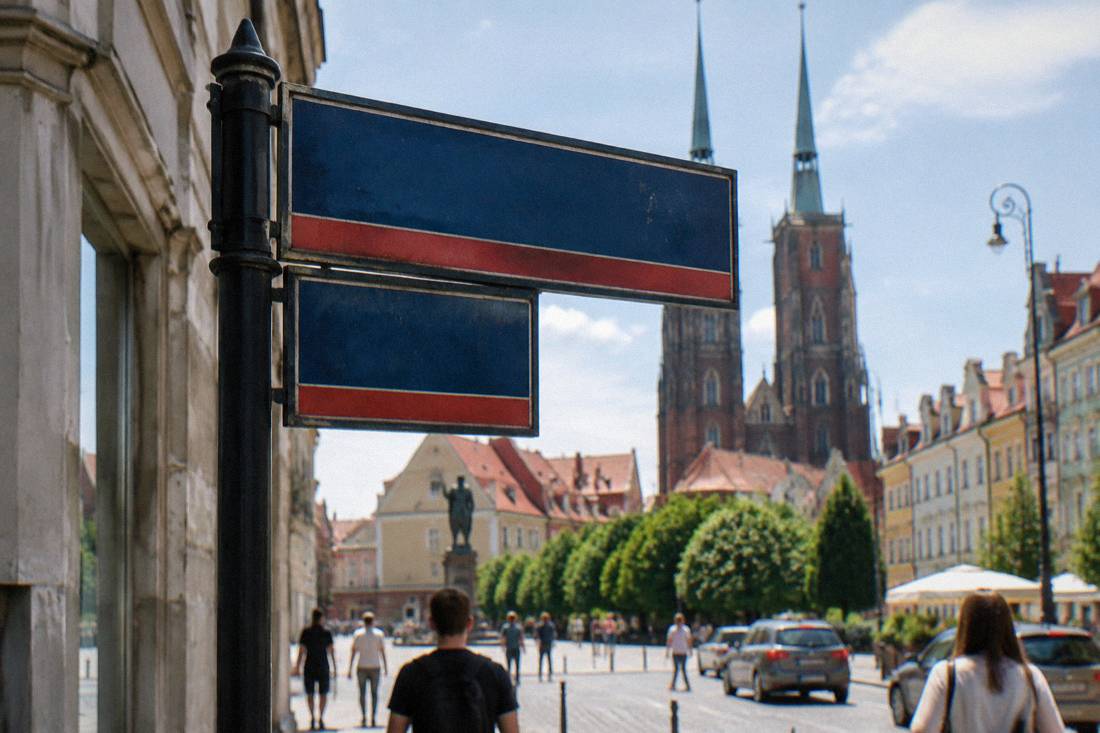 A close-up of a bilingual street sign showing a Polish place name in the city center
