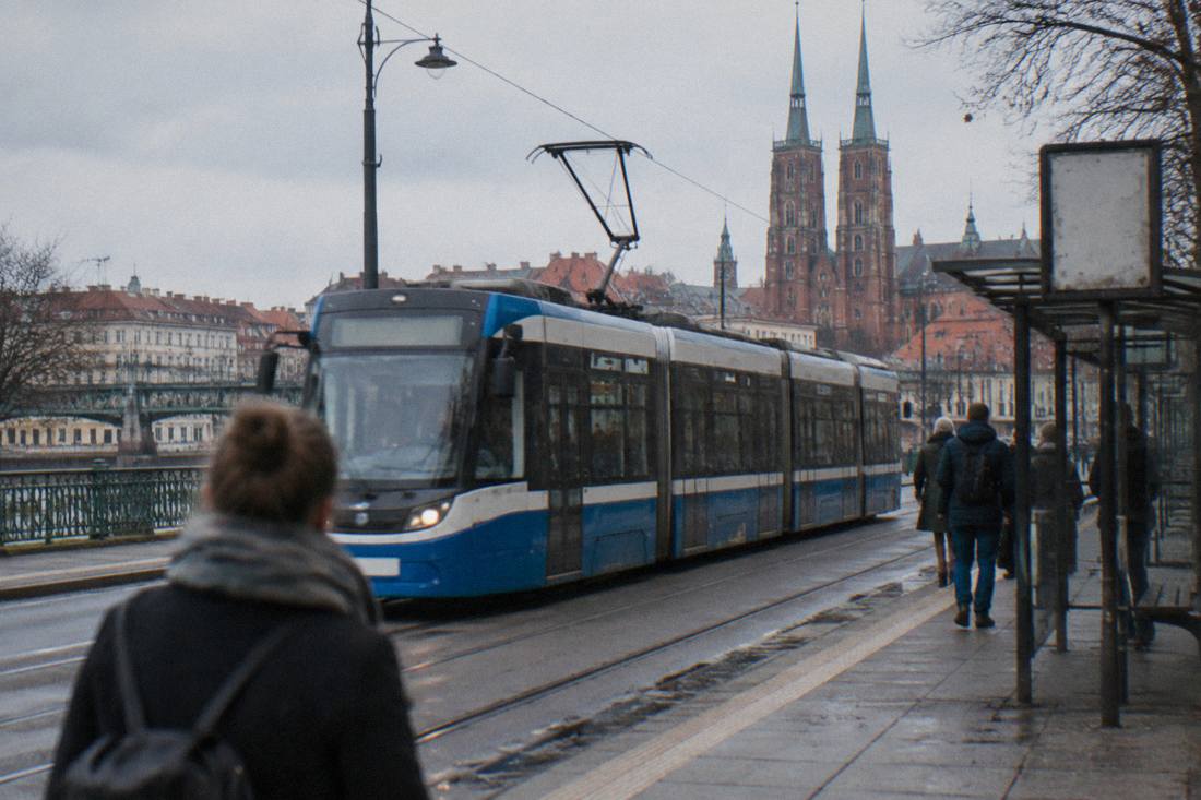A modern tram moving past a stop with Polish signage on a street in Wroclaw