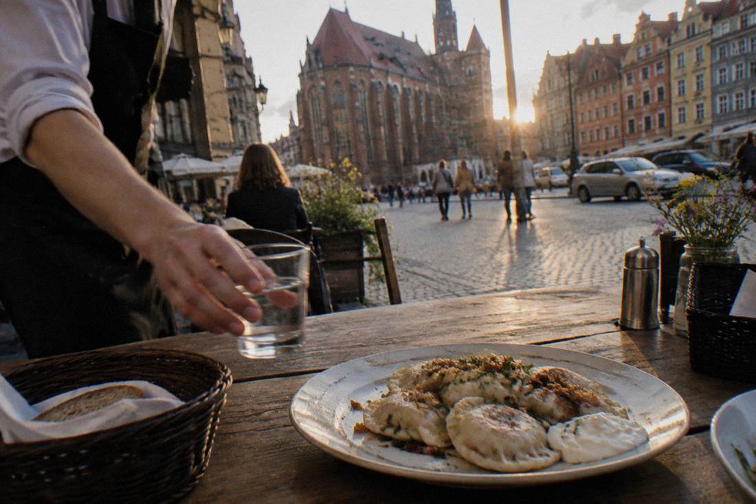 A waiter setting a glass of water beside a plate of pierogi on a restaurant table in Wroclaw