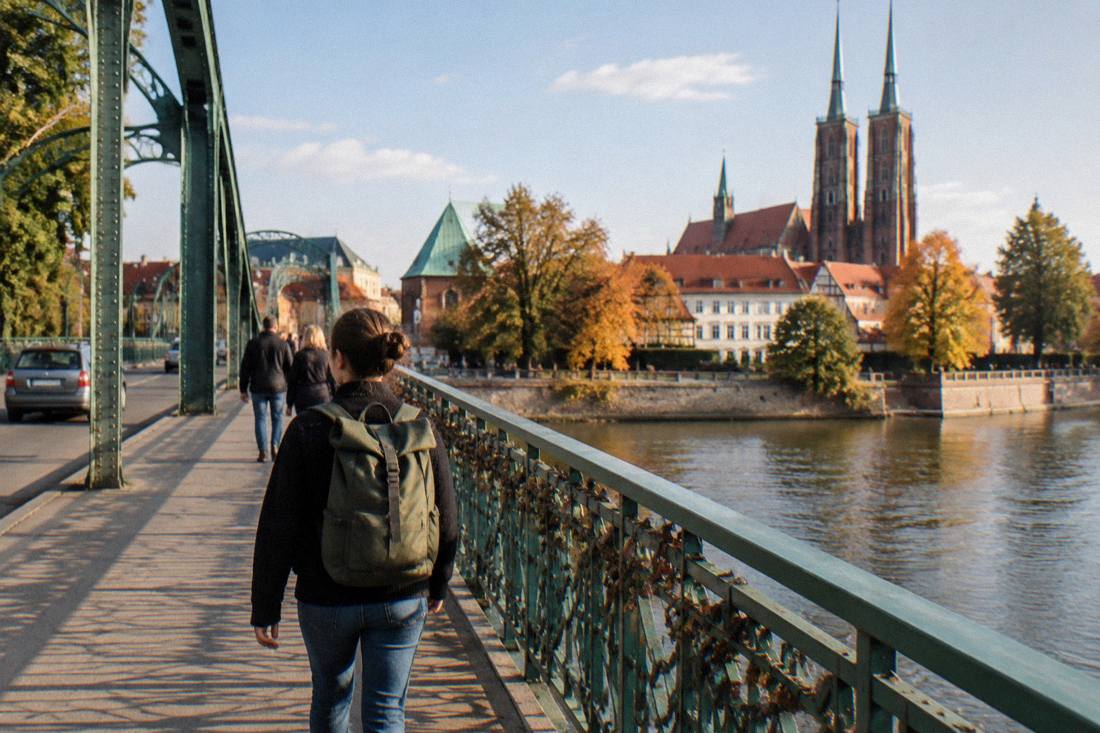 A traveler with a daypack crossing a Wroclaw bridge over the Odra on a warm afternoon