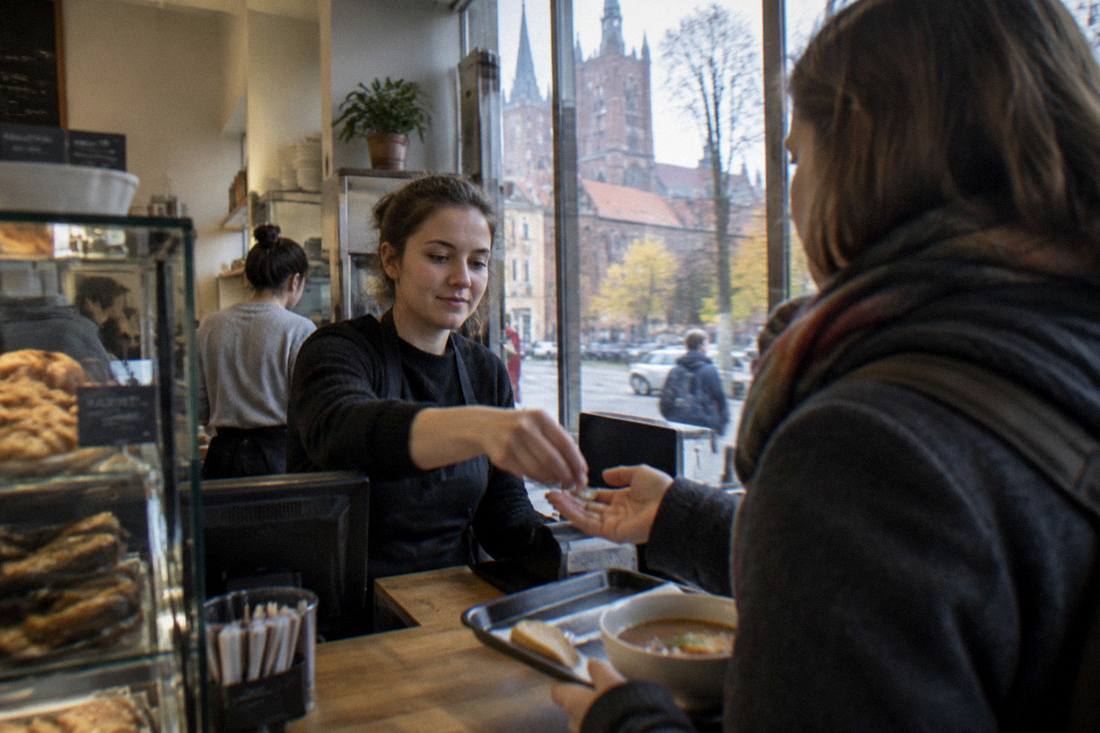 A cashier at a small cafeteria register handing change to a customer holding a food tray