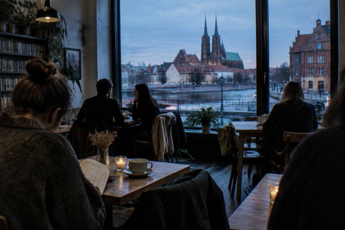 A cozy Wroclaw cafe interior with people reading and talking at wooden tables
