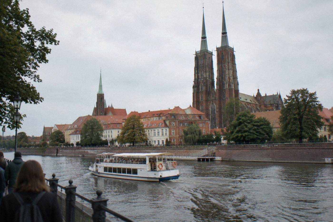 A passenger boat cruising on the Odra river past Wroclaw's cathedral island embankments