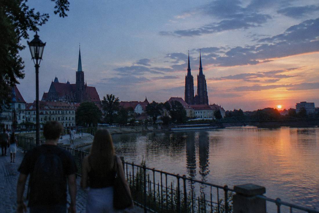 A summer sunset over the Odra river with the silhouettes of Wroclaw's old town rooftops