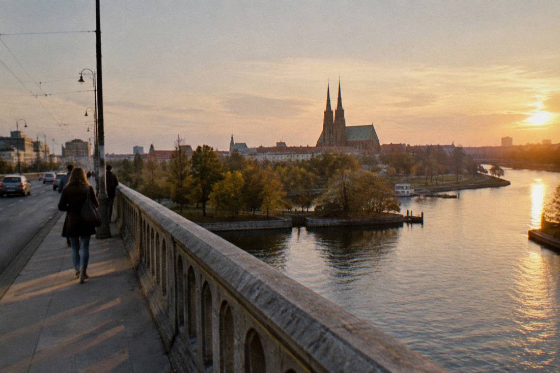 A stone bridge over the Odra river with the cathedral visible in the distance at golden hour