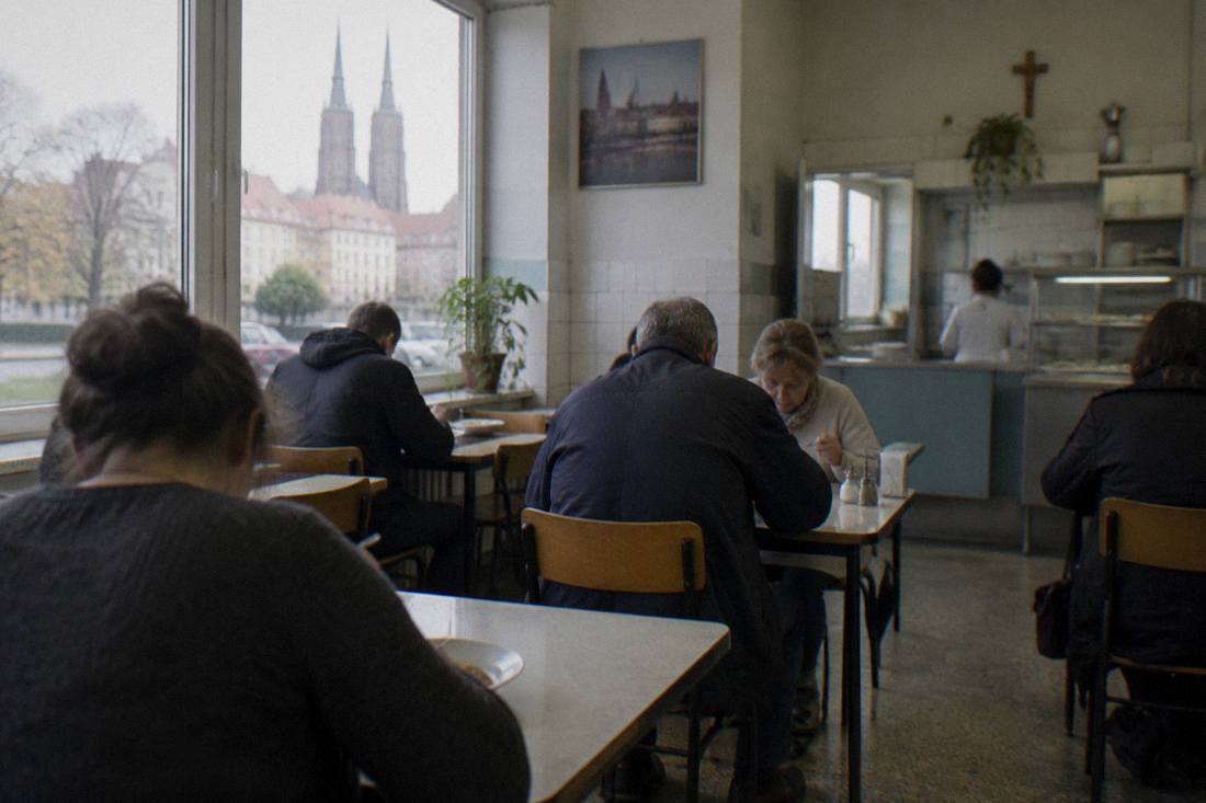 Diners eating lunch at small tables inside a simple Polish milk bar