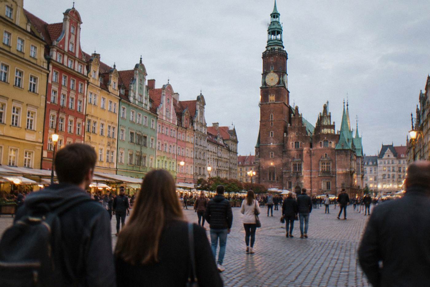 A market square in Wroclaw with colorful townhouses and people walking in the evening