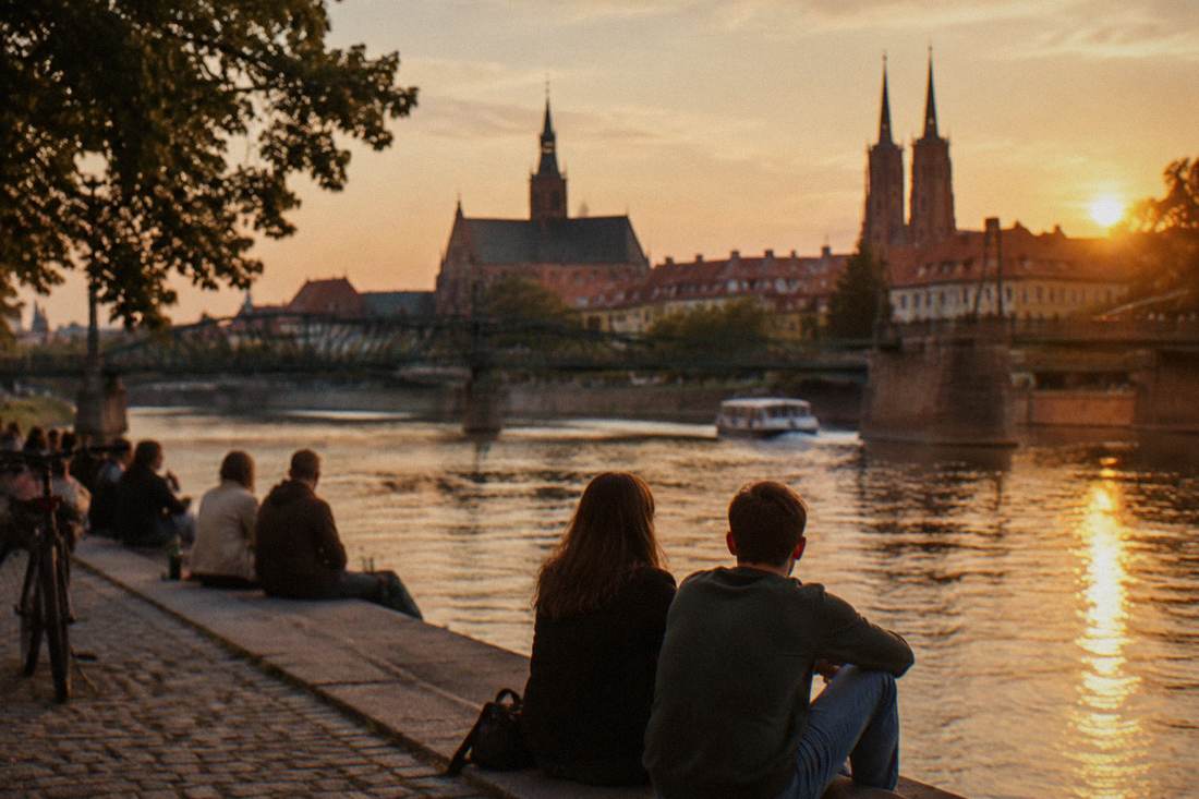 People sitting on a riverside embankment between bridges on the Odra in Wroclaw at golden hour