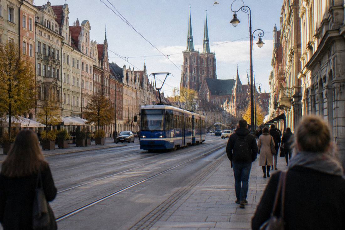 Trams and pedestrians on a wide street in central Wroclaw with historic facades on both sides