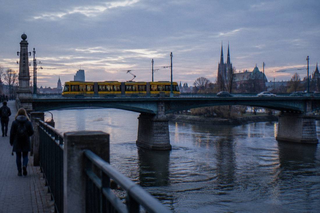 A yellow Wroclaw tram crossing a bridge over the Odra river on a quiet morning