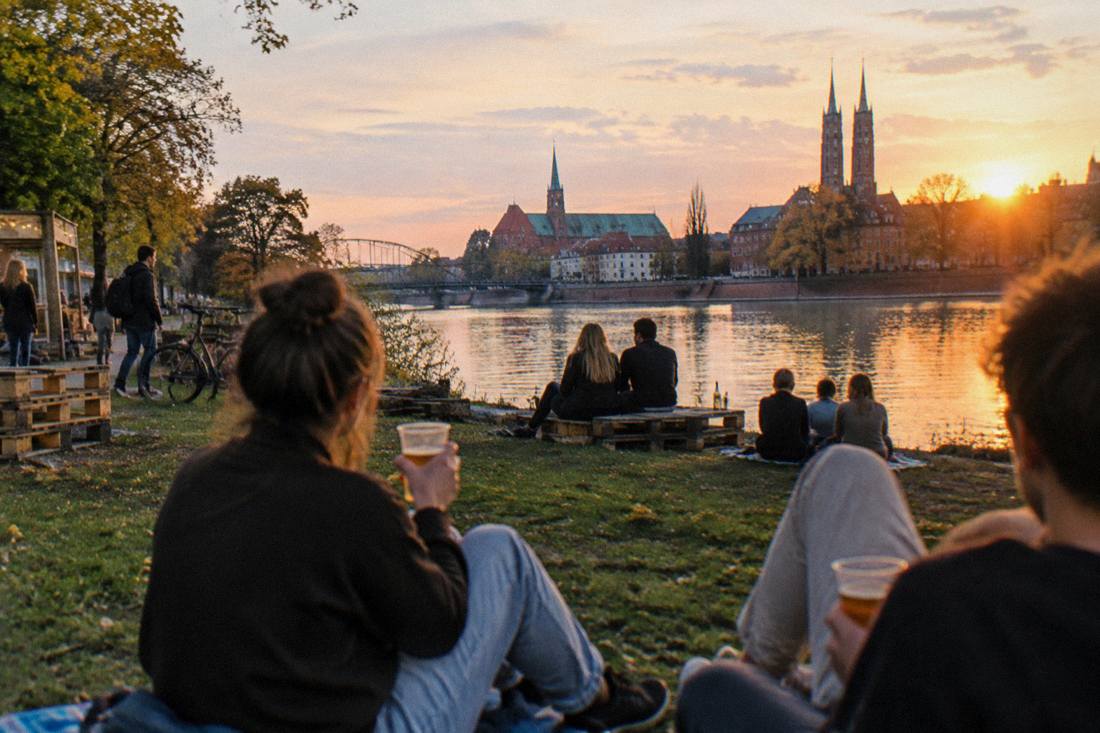 People relaxing with drinks on Slodowa Island by the Odra river in Wroclaw at sunset