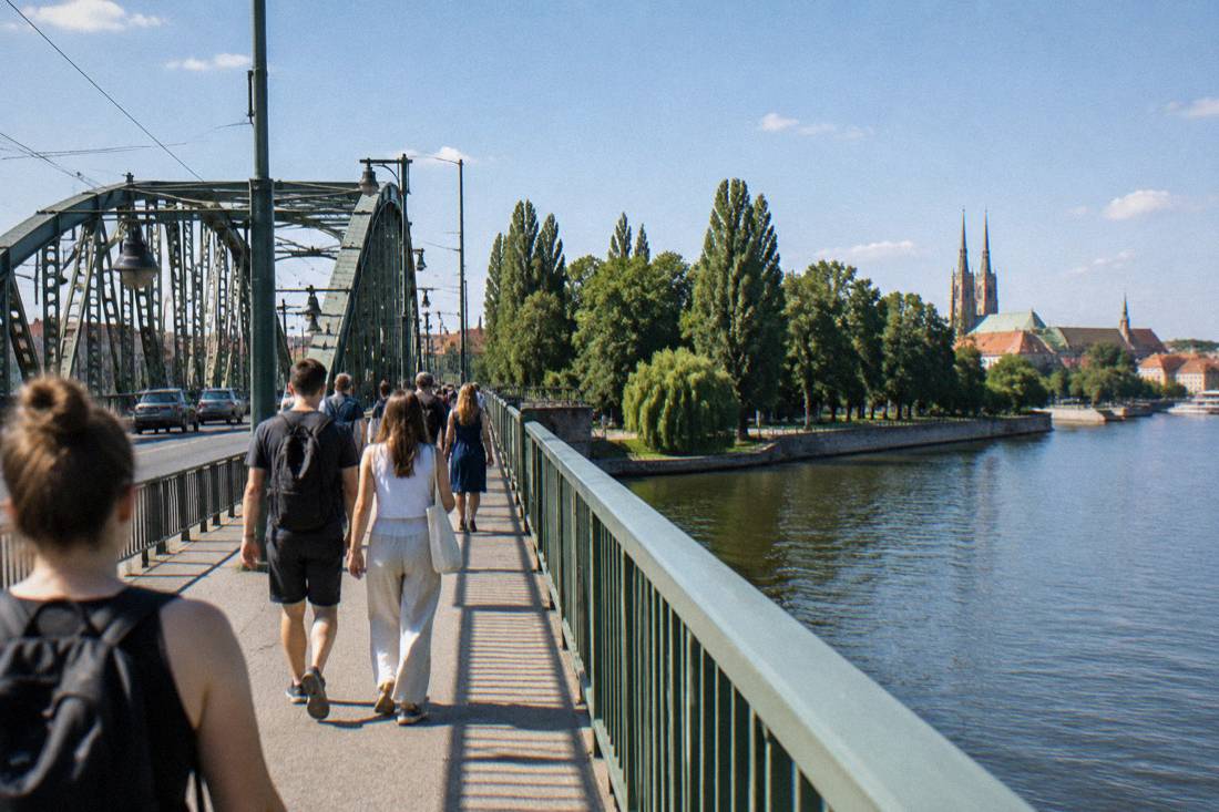 Pedestrian bridge over the Odra river in Wroclaw with people walking toward a tree-lined island