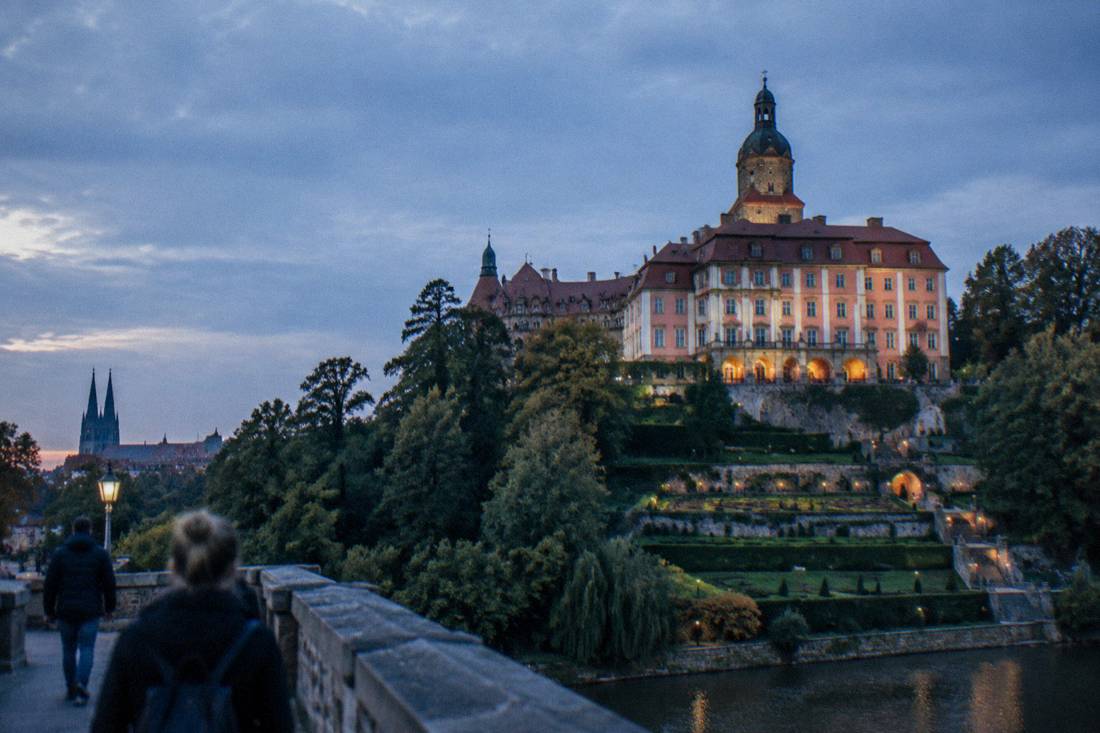 Large baroque castle on a forested hill with terraced gardens below