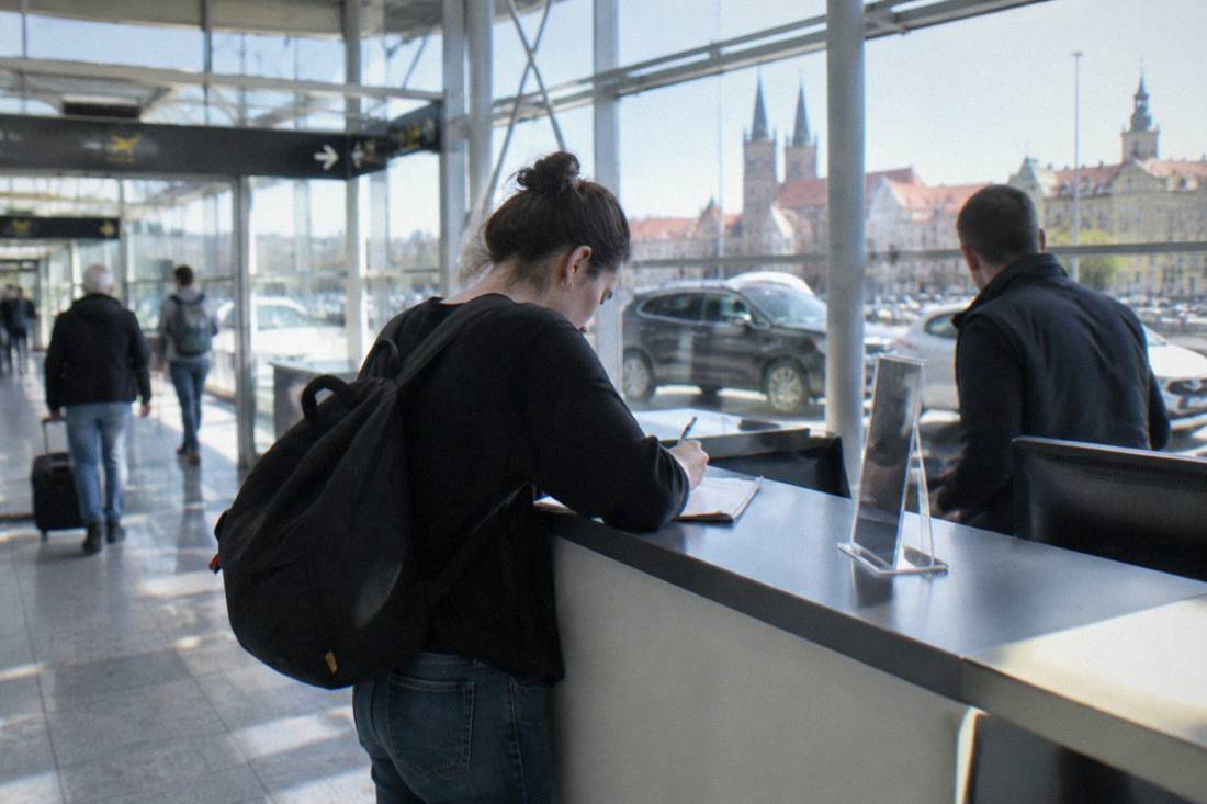 A customer signing paperwork at a car rental desk in an airport arrivals area.