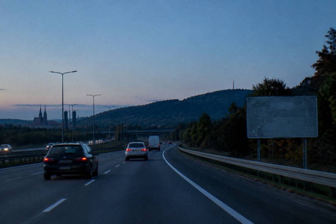A highway leading toward forested hills with a road sign and clear sky.