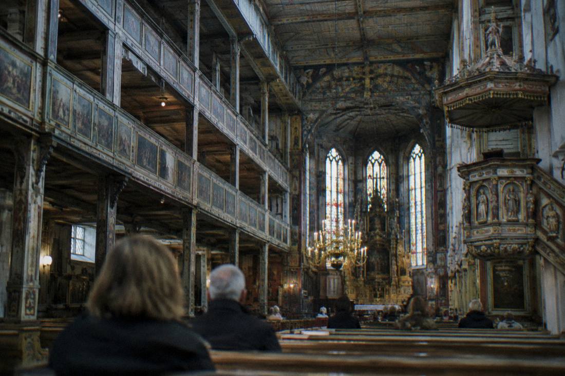The painted timber interior of a large historic church with wooden galleries and a pulpit.