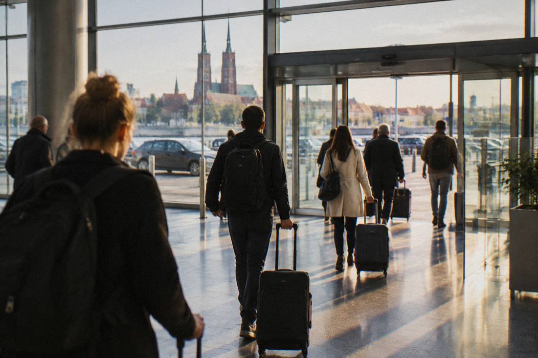 Travelers with suitcases walking through a bright airport arrivals hall toward exit doors