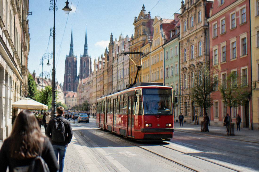 A red city tram moving along a street lined with colorful townhouse facades in Wroclaw