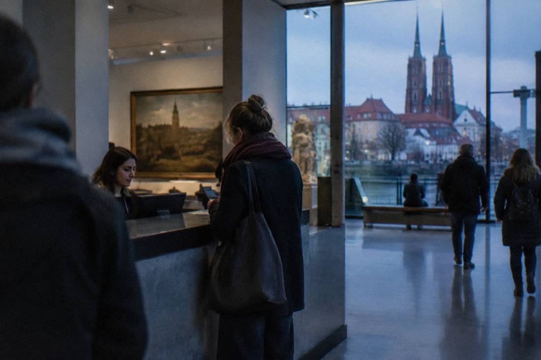 A visitor buying a museum admission ticket at a counter in a gallery lobby