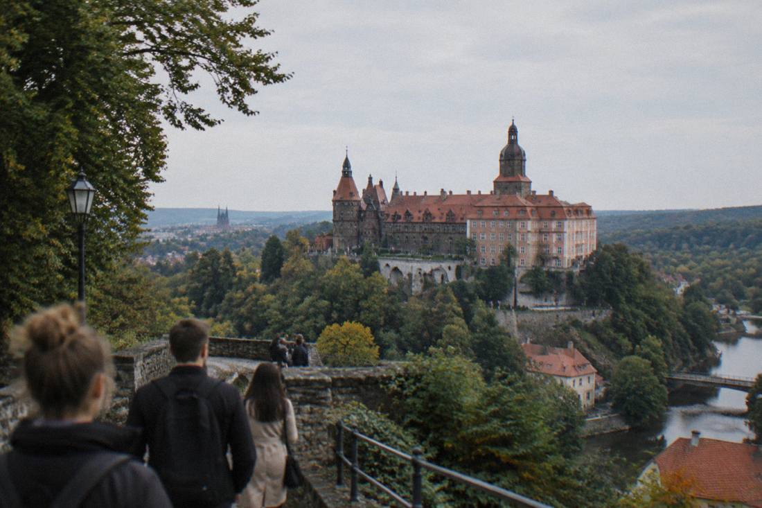 A large hilltop castle with towers and terraces overlooking forested hills in Lower Silesia